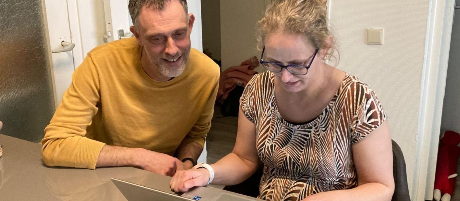 een vrouw zit achter een laptop met naast haar een ambulante begeleider