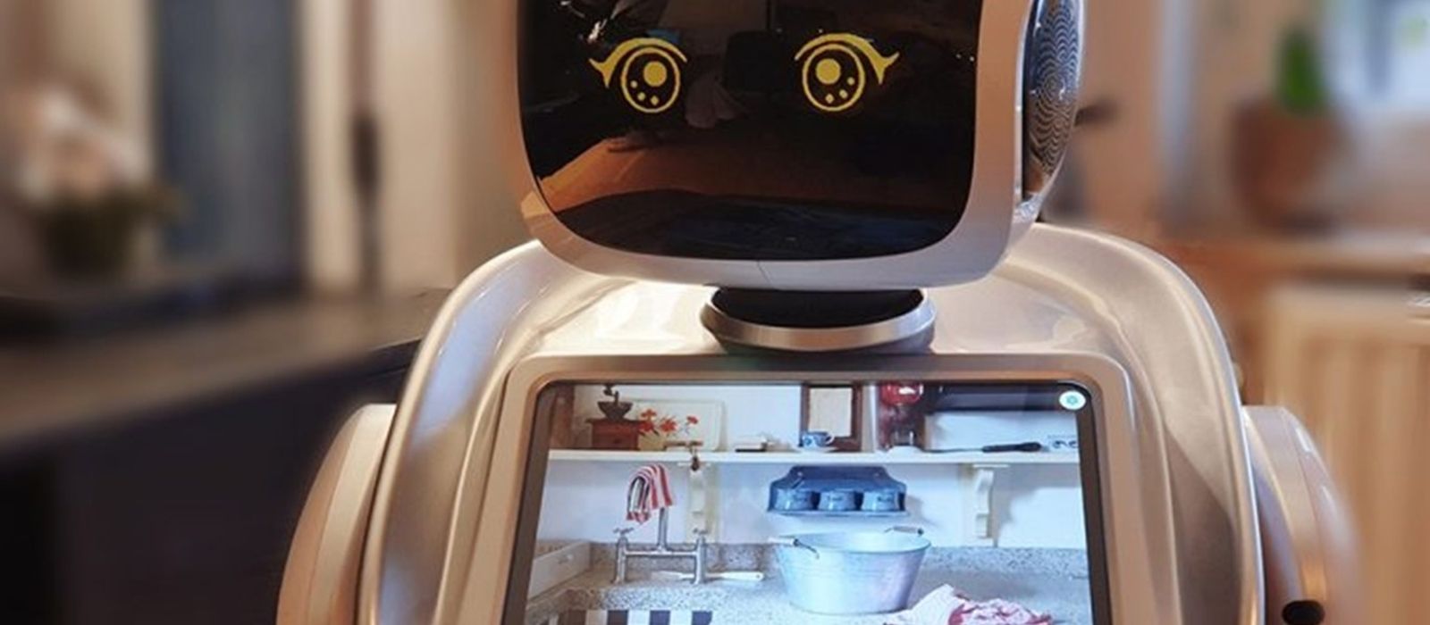 Een witte kunststof robot met een zwart gezicht en vrolijk gestemde ogen met in de borstkas een tablet verwerkt met een afbeelding van een keuken.