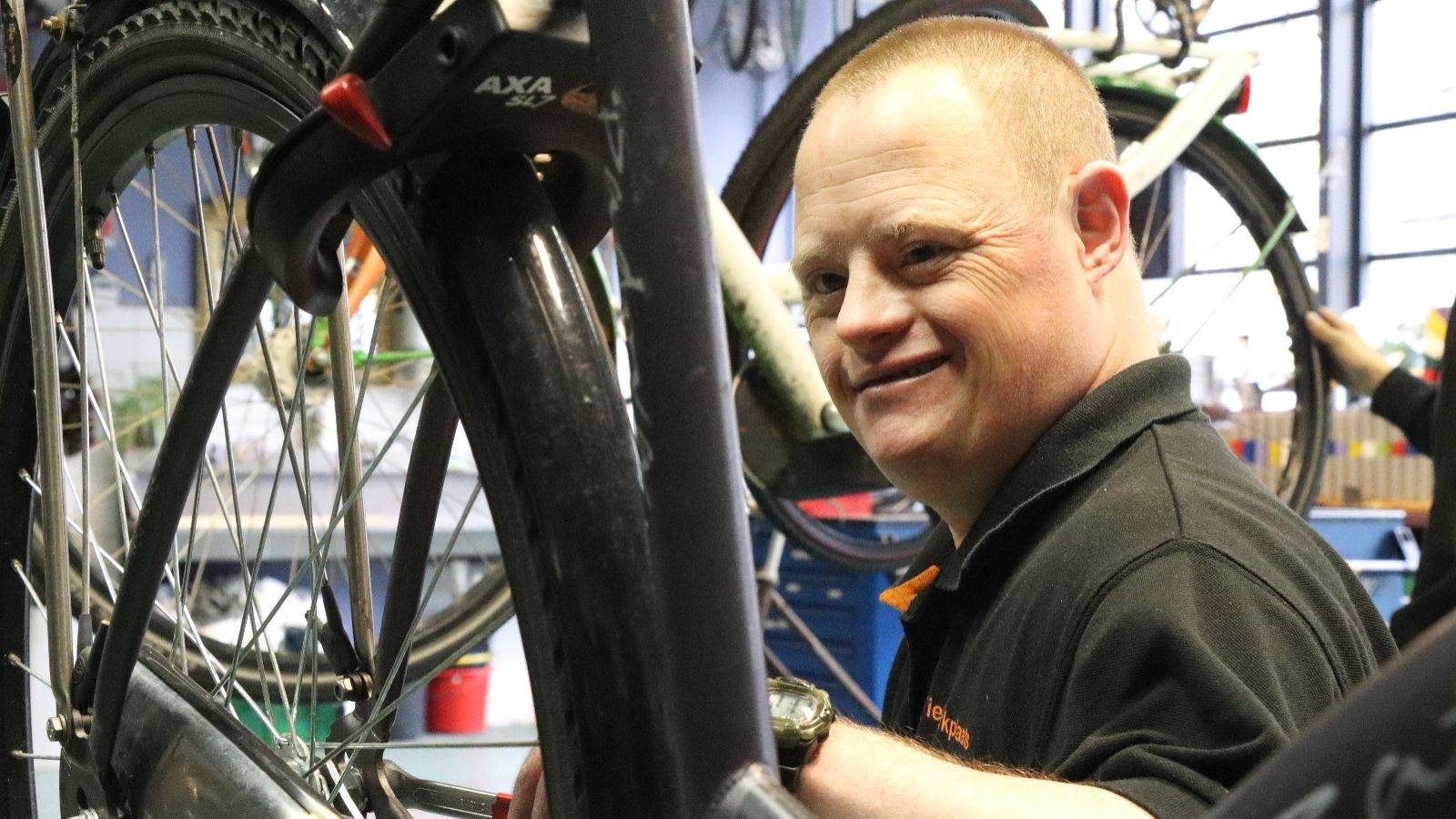 Een medewerker van de Brik-Fit repareert een fiets